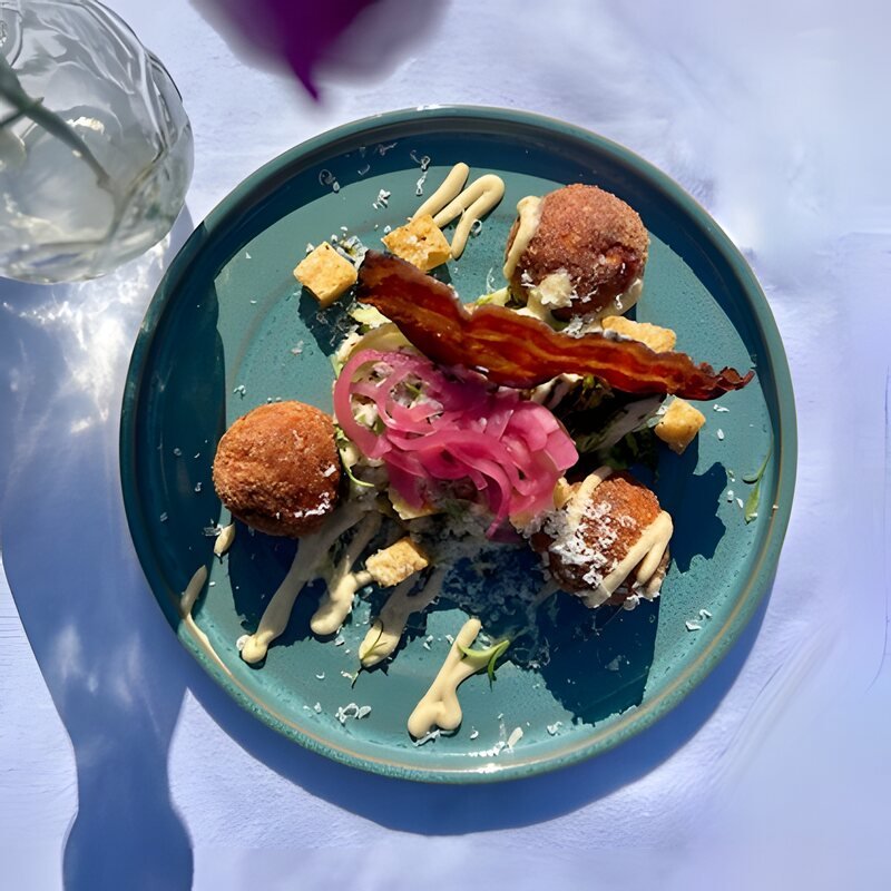 Voorgerecht op een blauw bord met kroketjes, spek en ingelegde rode ui